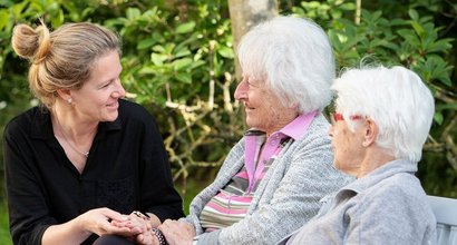 Seniorinnen sitzen mit einer Pflegerin im Garten