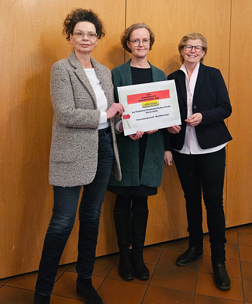 Drei Frauen halten einen Spendenscheck.