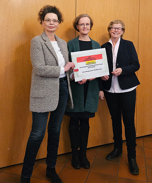 Drei Frauen halten einen Spendenscheck.
