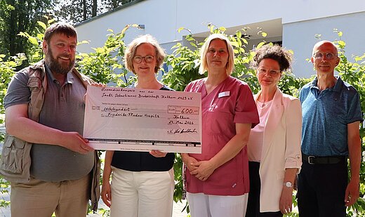 Eine Schaeckübergabe: Zwei Männer stehen links und rechts und überreichen an drei Frauen einen symbolischen Scheck in Höhe von 600 Euro. 