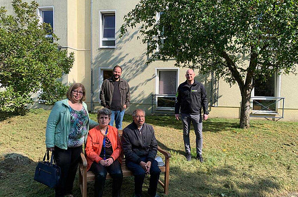 Eine Frau und ein Mann auf einer Gartenbank mit weiteren Personen