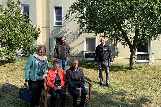 Eine Frau und ein Mann auf einer Gartenbank mit weiteren Personen