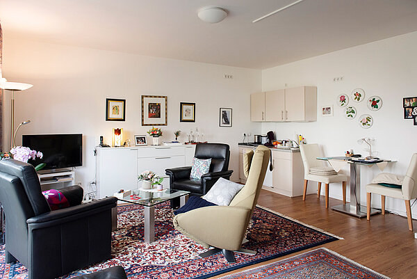 Ein Appartement mit Sesseln, Esstisch, Sideboard, Küchenzeile