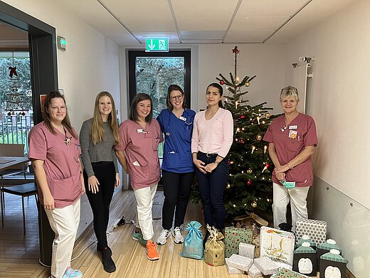 Sechs Frauen mit Päckchen an einem geschmückten Weihnachtsbaum