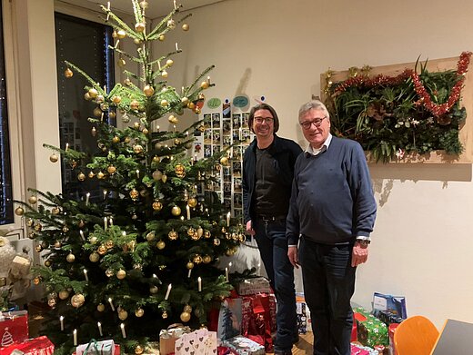 Zwei Männer mit vielen Päckchen neben einem Weihnachtsbaum