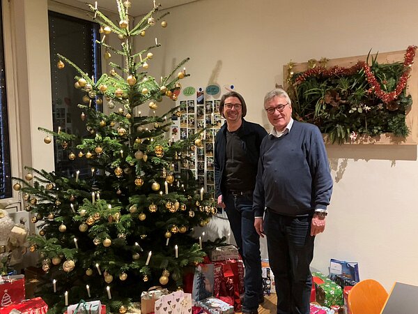 Zwei Männer mit vielen Päckchen neben einem Weihnachtsbaum