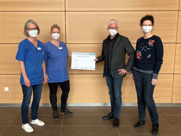 Vier Personen mit FFP2-Maske halten einen Spendenscheck.