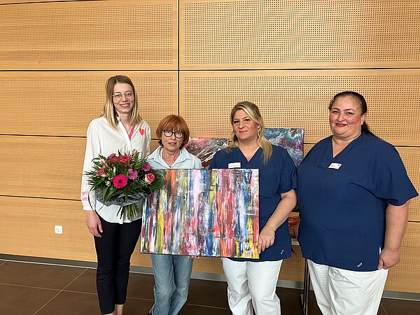 Vier Frauen mit einem Gemälde und einem Blumenstrauß