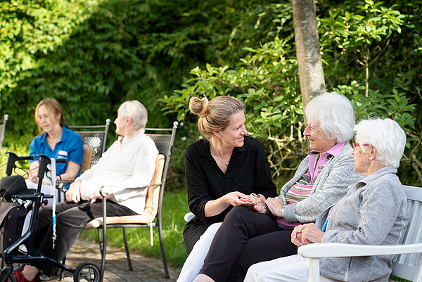 Mitarbeiterinnen und Seniorinnen sitzen im Gespräch im Garten