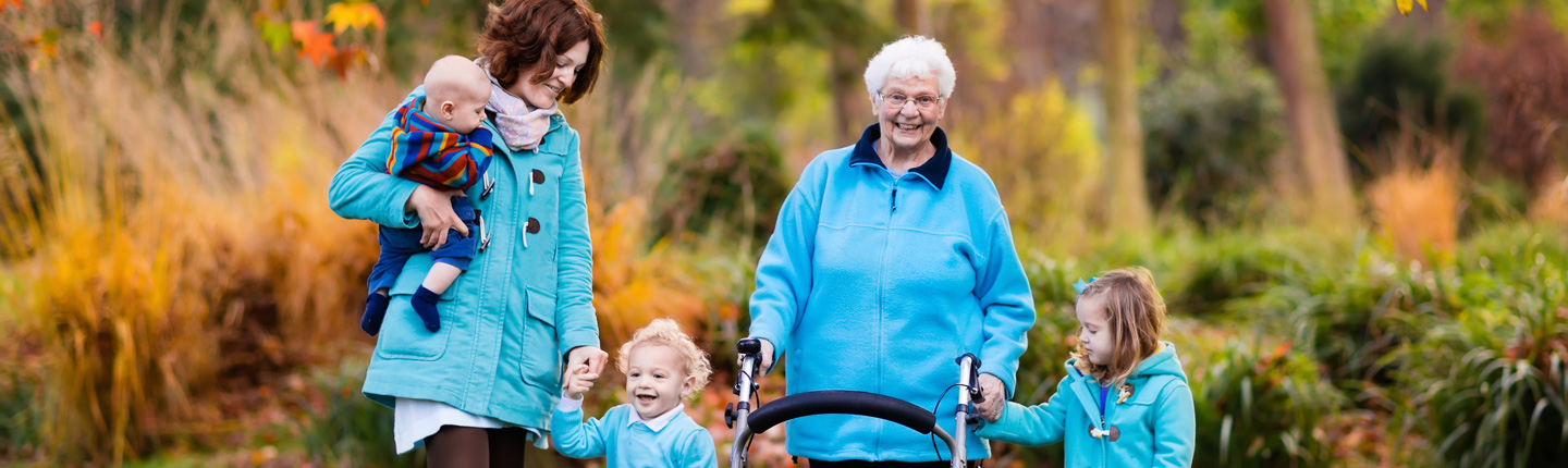 Mehrgenerationen: Ältere Frau geht mit ihrer Tochter und drei kleinen Kindern an einer Gehhilfe spazieren